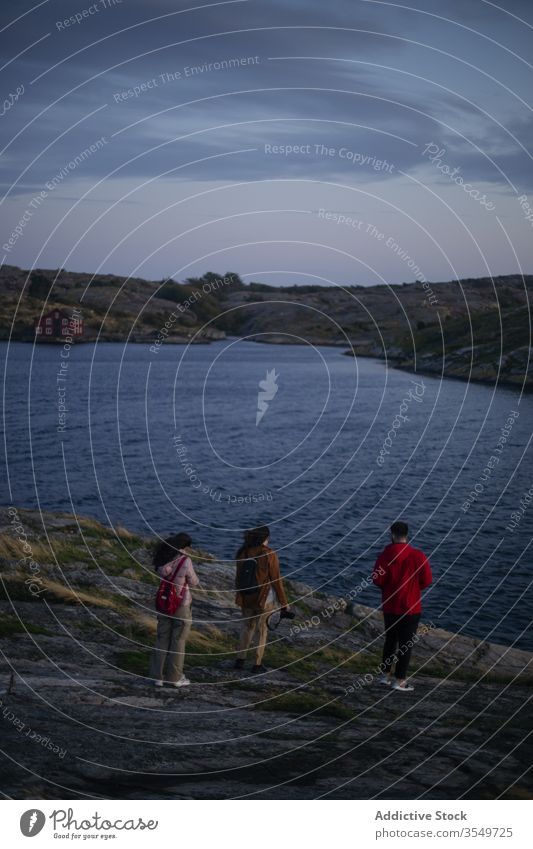 Unrecognizable couple walking down cliff to water traveler rocky coast evening sea photo camera together nature trip wanderlust journey tourism adventure