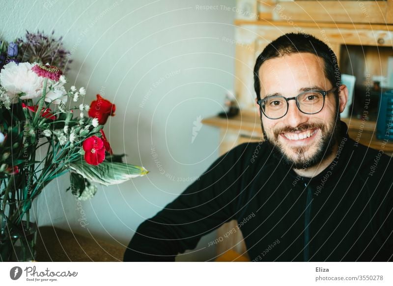 A man smiling friendly into the camera sits at home at the table next to a colourful bouquet of flowers Man smile kind Bouquet variegated son-in-law Son