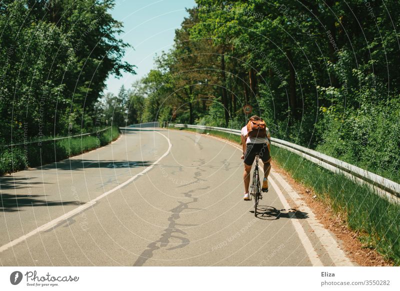 A man rides uphill on a bicycle on the road. Riding a bike. Trip. Cycling Summer Driving Bicycle out Sun hillock Incline Tall Sports Nature Man Street Lifestyle