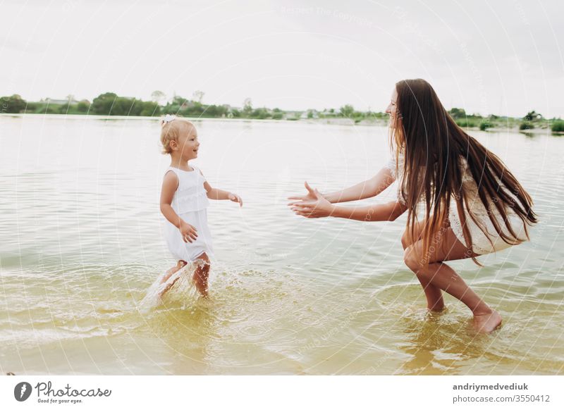 beautiful mother with baby daughter are having fun and playing near the lake. The concept of summer holiday. Mother's, baby's day. Spending time together. Family look. Sun light. selective focus