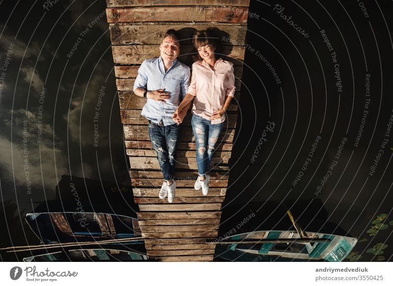 Beautiful young couple lies on a wooden bridge on the lake, looks lovingly at each other and smiles. Love story. beautiful people together lifestyle family