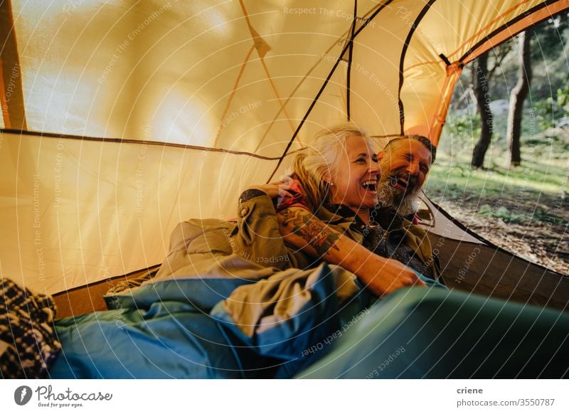 Senior couple laughing and cuddling inside tent in bedroll laying down smile happy enjoying active activity tourist leisure holiday seniors travel backpack