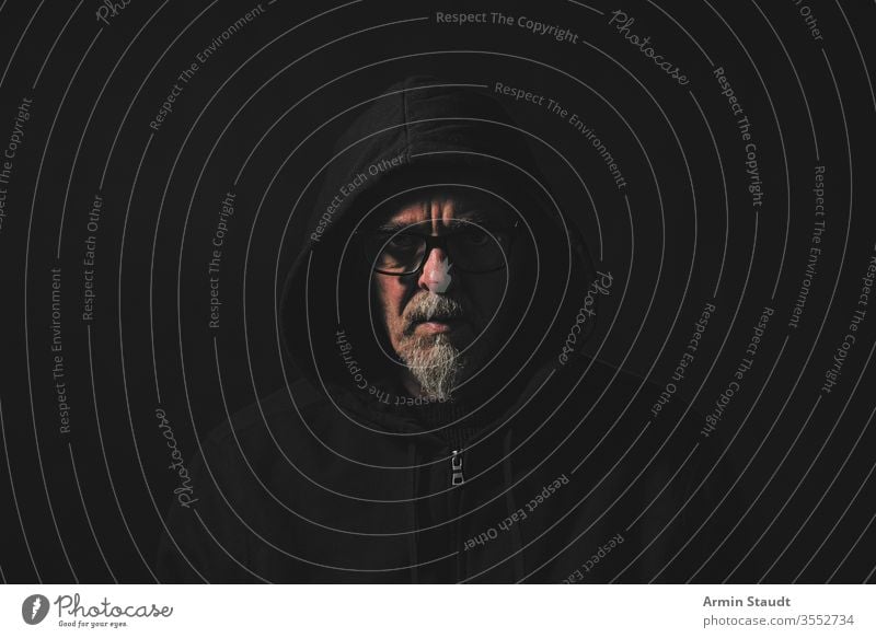 dark portrait of a man with gray beard , hoodie and glasses angle black blur casual caucasian close-up closeup confident cool danger dramatic emotion expression