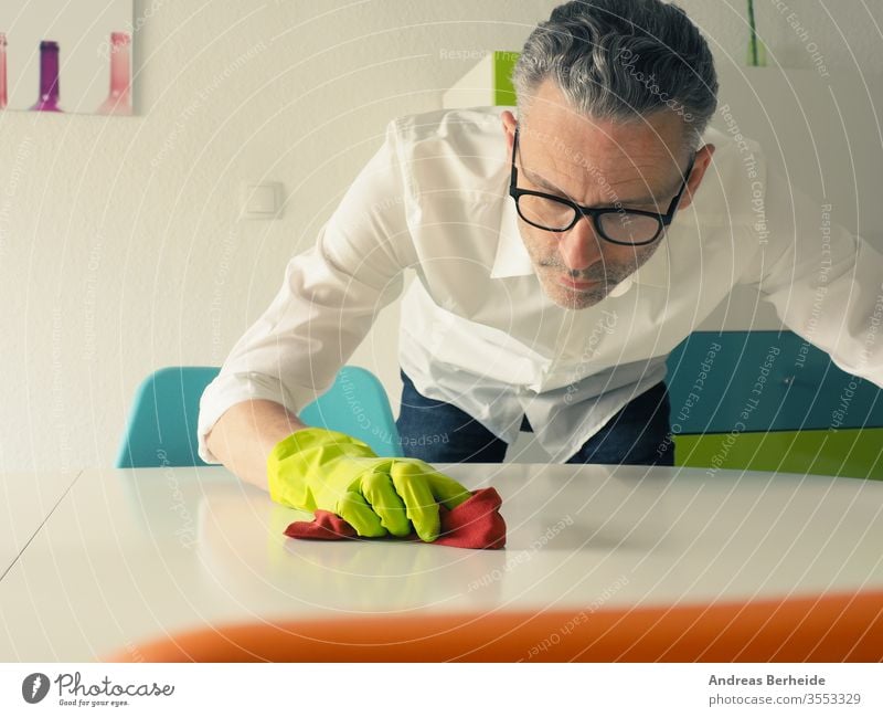 Middle-aged man thoroughly cleans a white dining room table cleaning perfection husband real indoors clear lifestyle manual cleansing concentrated truthful