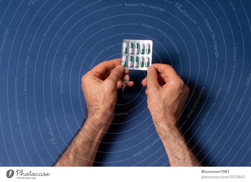 A man hands holding a small loaf of capsule pills in front of dark blue background single by fingers male people touch care treatment industry product human