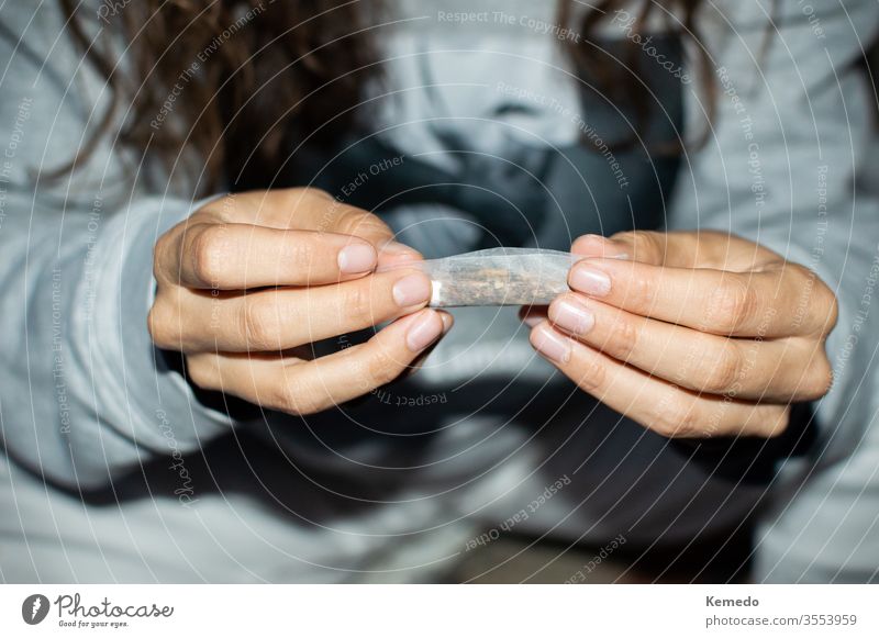 Young woman in tracksuit rolling a marijuana joint in the street at night. Details of hands rolling cannabis cigarette. girl young person teen smoke detail