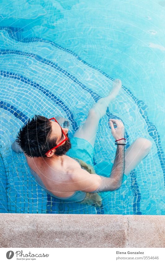 Top view of sexy young man with beard and red sunglasses sitting on the pool steps. Vacation concept. portraits men 1 having fun handsome hair relaxing naked