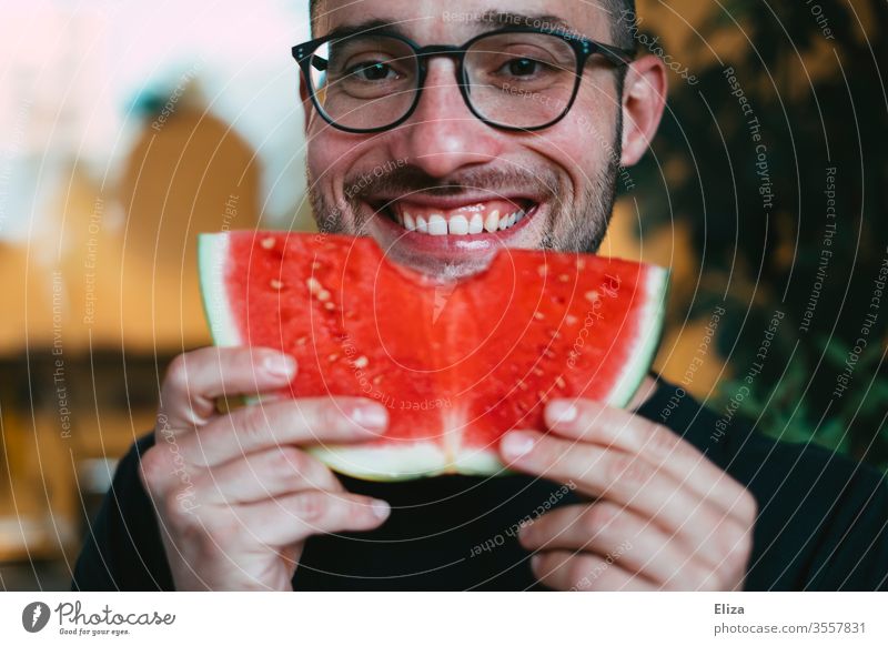 A man holds up a slice of watermelon that he has just bitten into and smiles Water melon bite into Bite Delicious Eating salubriously Fruity Man Joy feast fruit