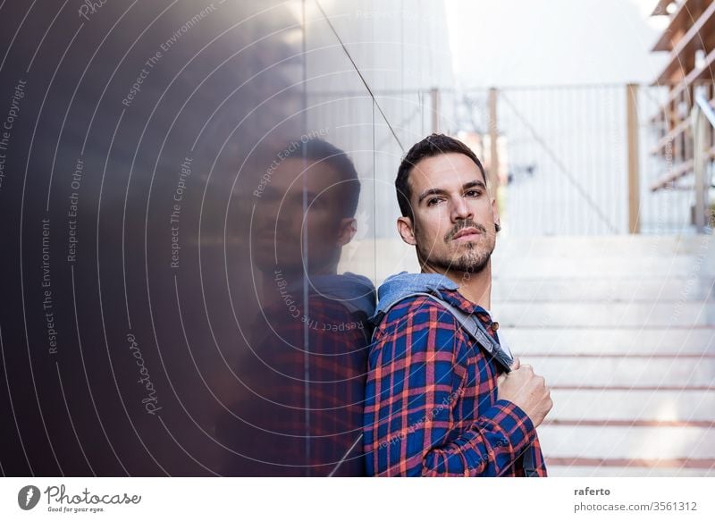 Young bearded man leaning on a dark wall holding a shoulder bag while looking away person adult young male attractive fashion guy background hair beautiful