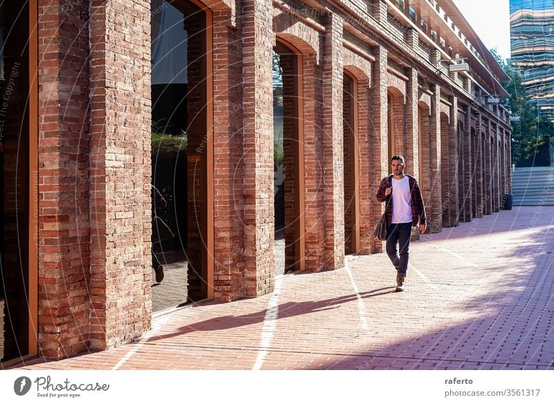 Bearded young male holding shoulder bag while walking in a business district adult man young adult outdoors people businessman beard portrait city one person