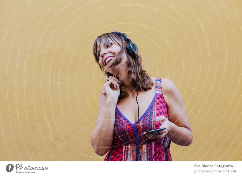 portrait of young caucasian woman outdoors over yellow background listening to music on headset and mobile phone. summer time technology app song people