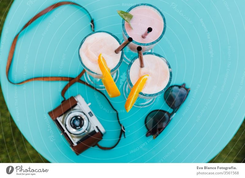 three colorful smoothie drinks, a vintage camera and sunglasses on a blue table on a terrace, summer time healthy juice fruit background nobody 3 orange iced