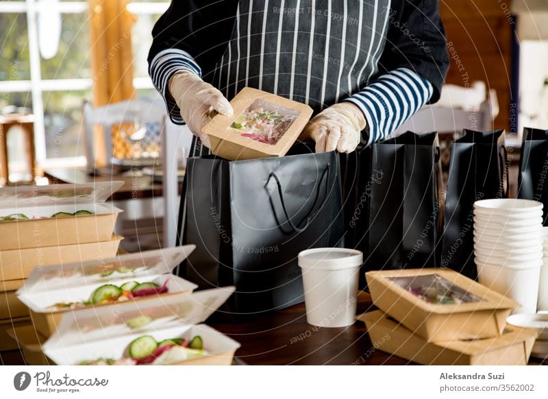 Restaurant worker wearing protective mask and gloves packing food boxed take away. Food delivery services and Online contactless food shopping. business buy