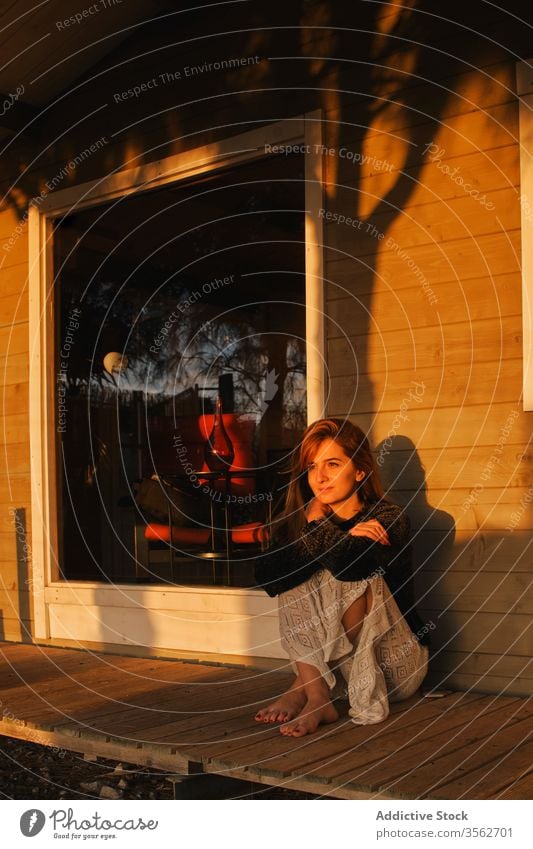 Delighted woman admiring sunset on terrace of wooden cabin admire relax veranda house delight barefoot female serene chill weekend countryside casual outfit