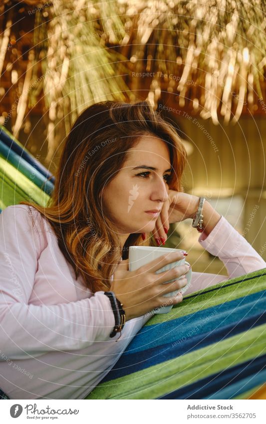 Relaxed woman with cup of coffee in hammock relax hot drink calm lying barefoot courtyard enjoy female summer holiday vacation weekend mug casual outfit