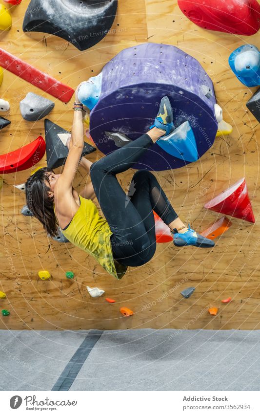 Powerful female boulderer practicing on wall climber woman sport training hang strong stamina workout power grip high hobby muscular equipment gym smile laugh