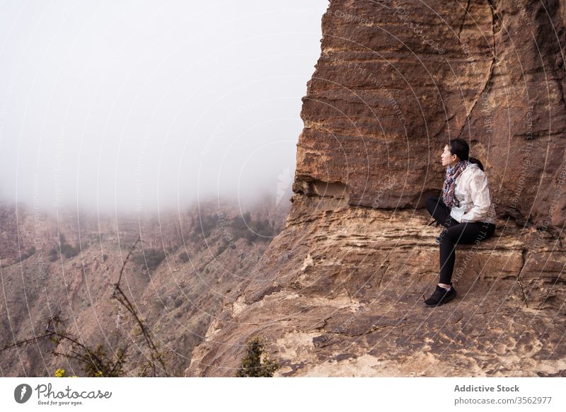 Ethnic traveler sitting on rock woman mountain fog explore ethnic rough nature female casual cliff journey asian adventure landscape trip freedom tourism lady