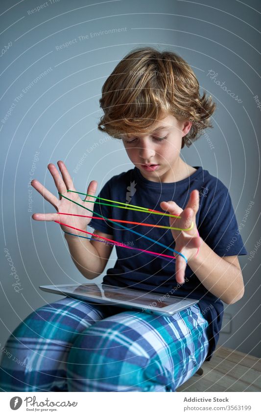 Child with tablet learning cats cradle game kid string play creativity figure stool pajamas home boy focus preteen tie imagination skill develop finger device