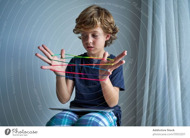 Child with tablet learning cats cradle game kid string play creativity figure stool pajamas home boy focus preteen tie imagination skill develop finger device