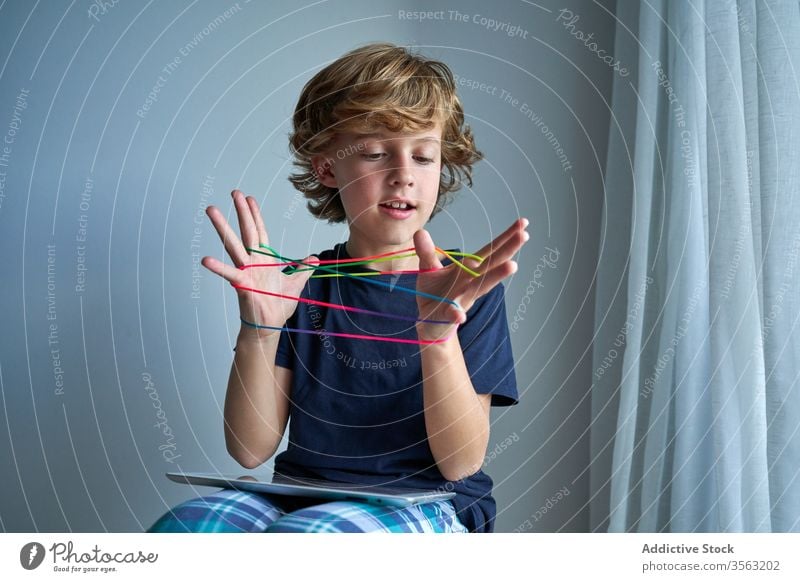 Child with tablet learning cats cradle game kid string play creativity figure stool pajamas home boy focus preteen tie imagination skill develop finger device