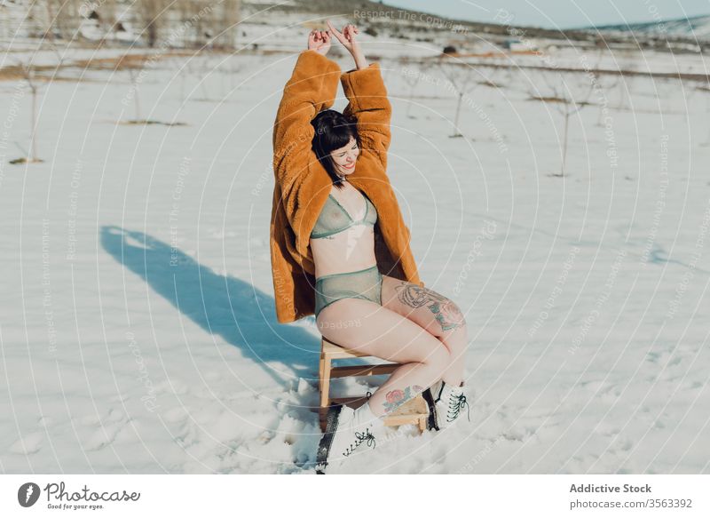 Young woman in fur coat and lingerie sitting in snowy field sensual nature winter brunette confident female trendy young slim style fashion lady attractive