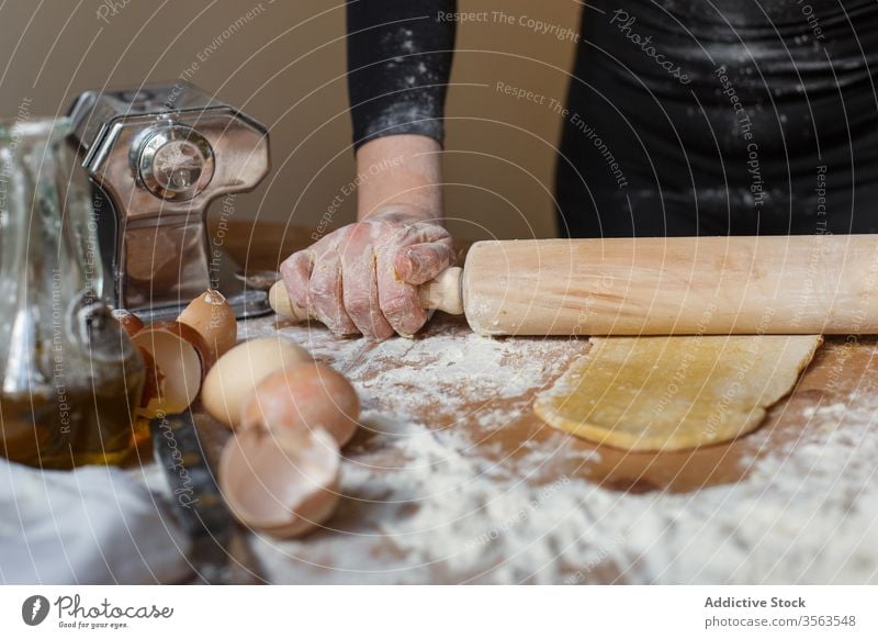 Crop lady rolling dough with rolling pin on table cook woman pastry elastic flour egg kitchenware jug eggshell glass prepare ingredient process pasta utensil