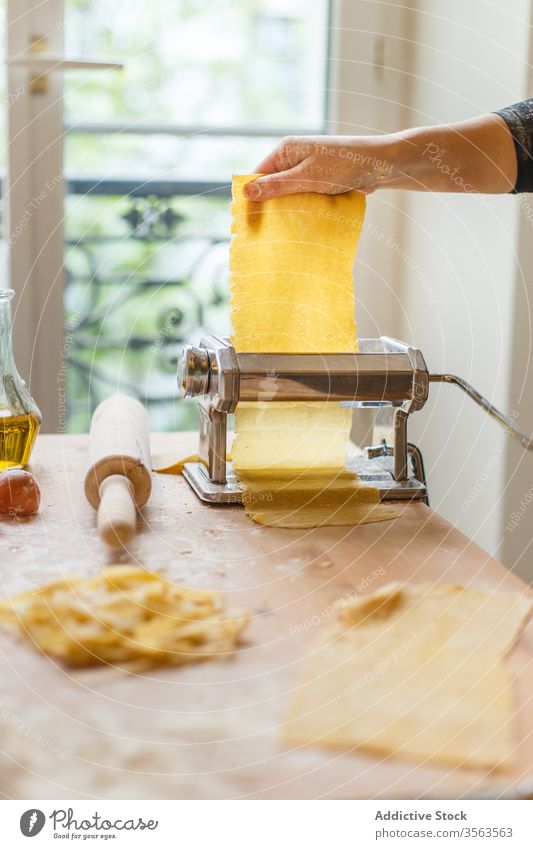 Anonymous female cook rolling dough while using pasta machine woman pastry elastic flour appliance kitchenware egg instrument glass whisk prepare eggshell