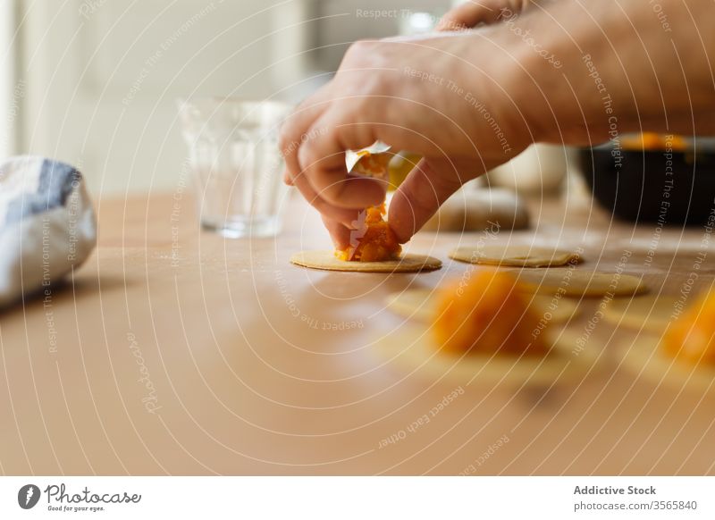 Crop person stuffing ravioli with pumpkin filling dough prepare circle cook table round wooden process kitchen food cuisine culinary homemade dish recipe