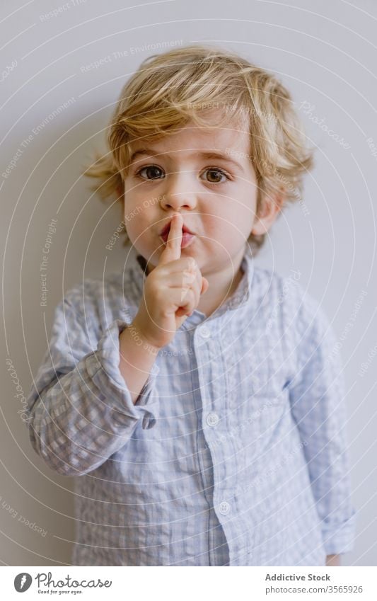 Adorable boy making silence gesture adorable index finger gesticulate little cute kid child content childhood casual face expression happy stand touch lips