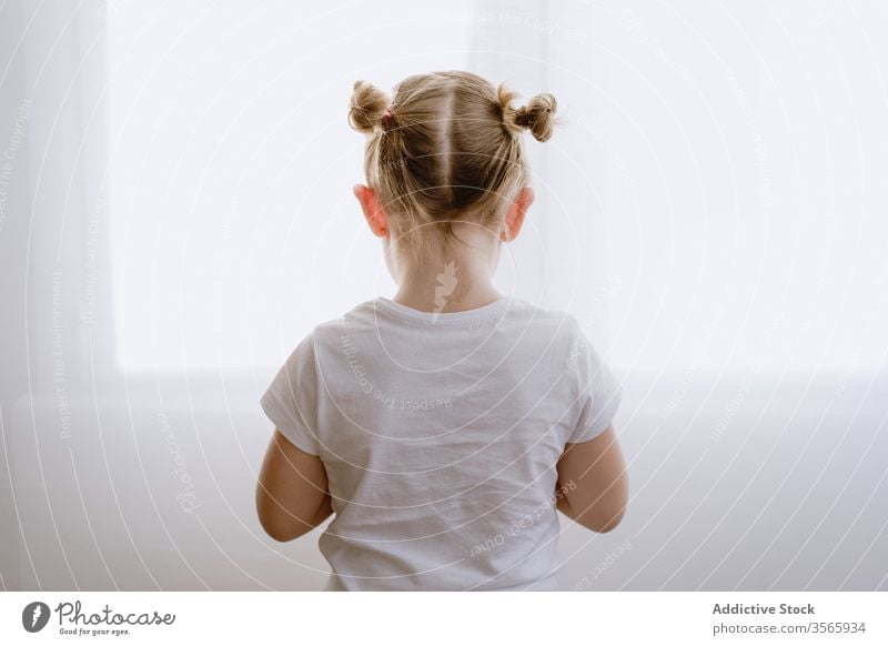 Anonymous little girl standing on white wall morning kid living room adorable child cute childhood window style bright apartment modern home casual outfit wear