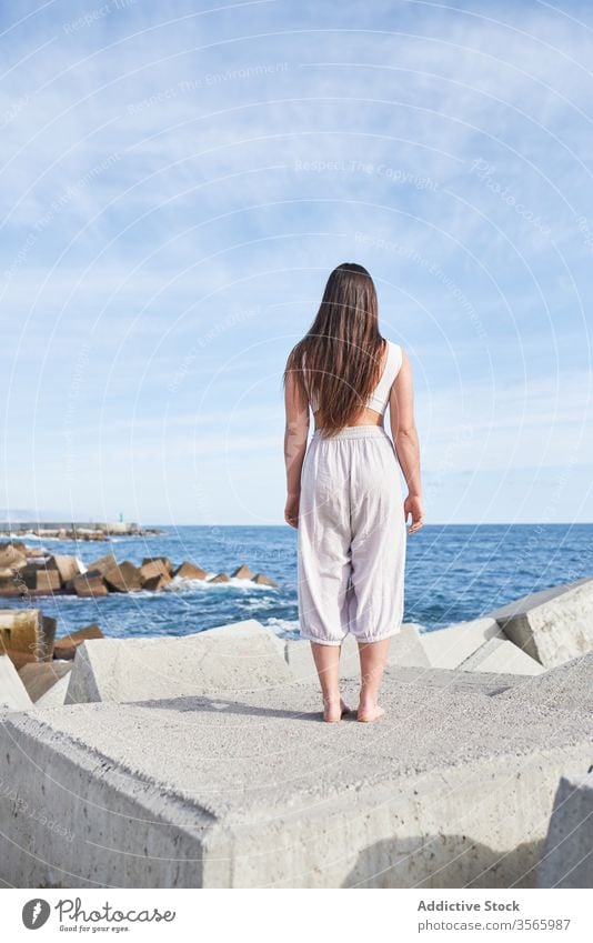 Anonymous modern woman standing on concrete block of breakwater sea harmony coast contemporary concept stone construction energy physical young pose female