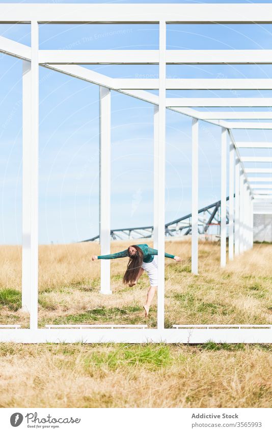 Young woman near metal construction in countryside field dance fall bend geometry fly modern street art nature harmony calm female creative contemporary frame