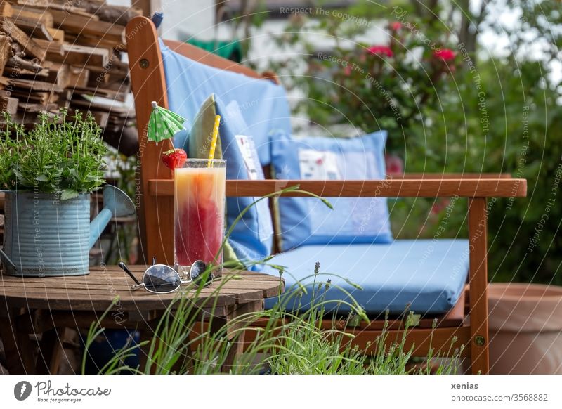 Kiba with drinking straw, strawberry and umbrella, sunglasses, as well as a garden bench with blue cushions are ready for a short break seat Garden bench