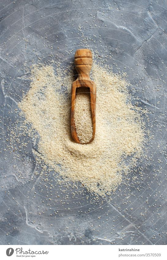 Raw uncooked fonio seeds with a spoon on grey background dry wooden top view african cereal food nutriment organic vegan vegetarian gluten free alternative