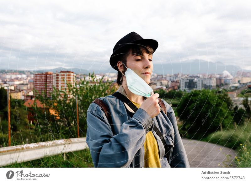 Serious young lady with medical mask standing on street in city woman breath urban covid19 fresh air serious coronavirus outbreak lockdown pandemic hat