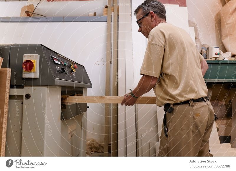 Careful pensive woodworker planing wood beam using machine in contemporary workshop master lumber grind carpenter processing man control artisan plane panel