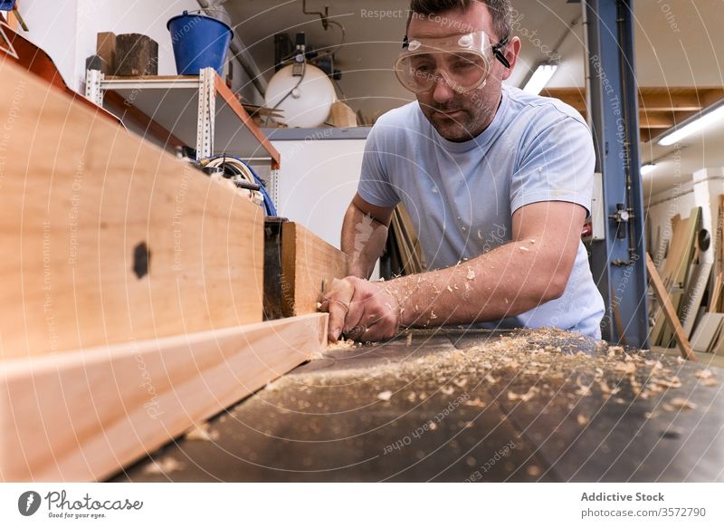 Skilled woodworker using milling machine while working with lumber in contemporary workroom carpenter glasses workshop sawdust safety man detail control timber