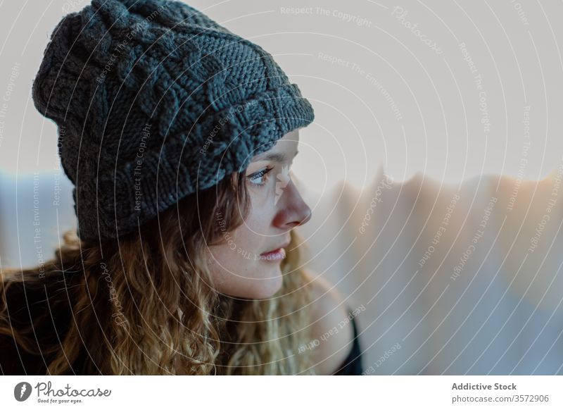 Tranquil young woman in hat looking away with interest and contemplating warm knitted dream melancholy think ponder contemplate watch wait pensive appearance