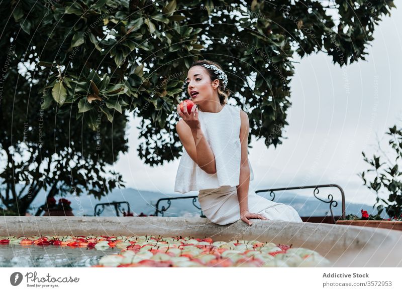 Young bride eating apple from fountain woman garden elegant young fresh wedding female bite model fruit water wet bowl summer park style sit attractive pretty