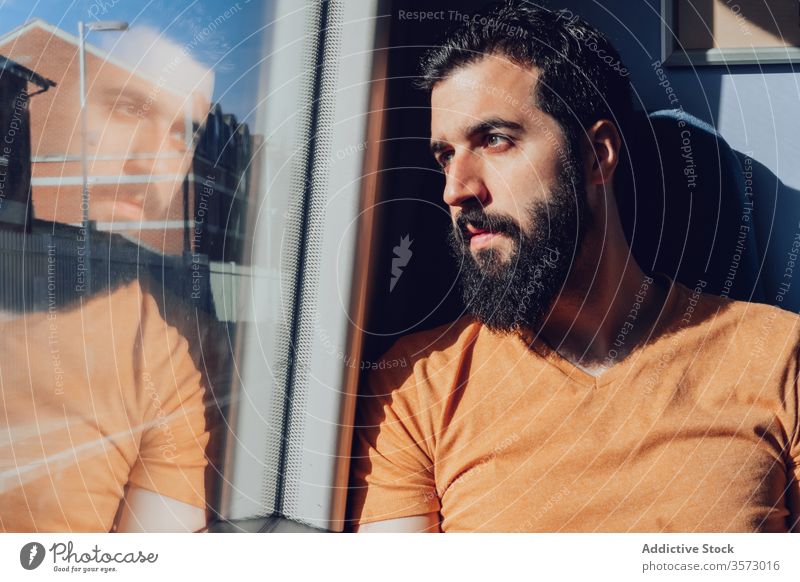 Thoughtful young bearded man looking through window while traveling by train trip dream pensive sunlight summer serious transport passenger seat alone