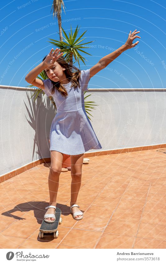 Pretty little girl in a striped dress playing with a skateboard on the terrace of her house look city happy cool clothes summer casual attire stylish fun