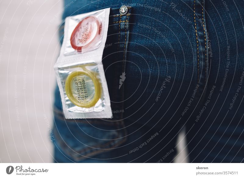 young guy in jeans is preparing for a romantic date-puts a colored condom in the back pocket of his jeans. Body part: male ass. Concept: protection against sexually transmitted diseases