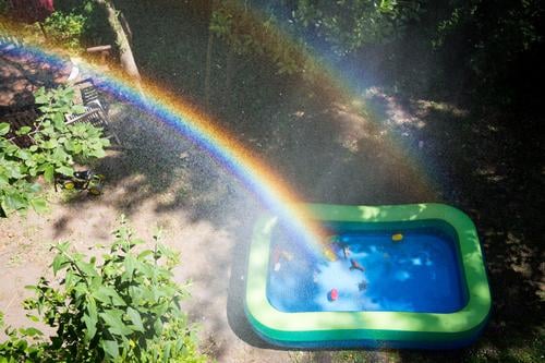 Rainbow over a paddling pool in a garden Garden Paddling pool Water Toys Drops of water spray mist Sunlight Infancy out Beautiful weather warm season Summer