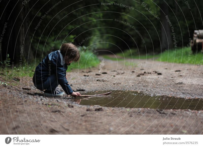 Child playing on a forest path by a puddle Forest Puddle huts Nature green Spruce forest Tree trunk Fir cone Grass Rain jacket Sneakers girl short hair Playing