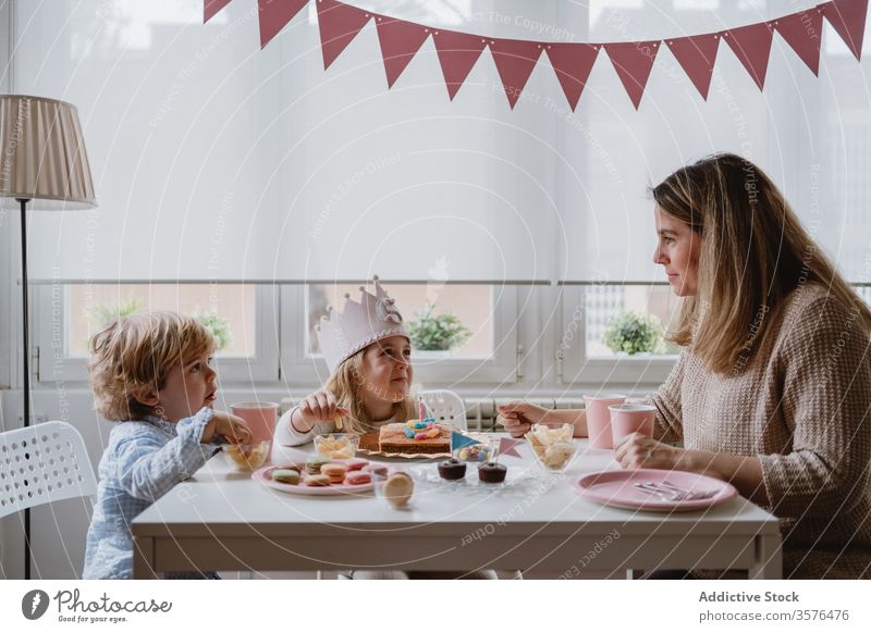 Positive mother playing with kids while having home birthday party children happy celebrate fun parent sibling girl boy together talk positive smile communicate