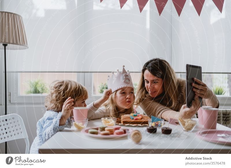 Cheerful little girl making video call on tablet during birthday celebration mother daughter celebrate fun happy remote home distance positive kid mobile phone