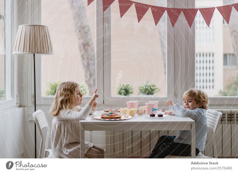 Little kids sitting at table near window in living room children home celebrate birthday cake sibling together garland cozy sweet holiday eat adorable occasion