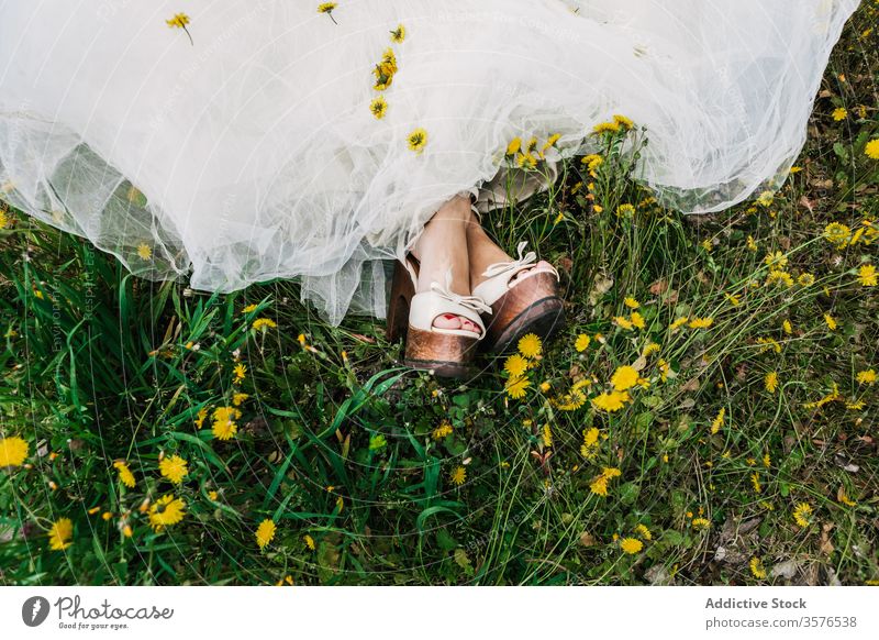 Crop bride in meadow with dandelions newlywed wedding day flower wedding dress high heels bloom female field blossom relax lawn calm tranquil serene sit