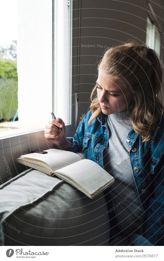 Pensive woman with notebook sitting near window diary home pensive young student notepad thoughtful read casual female think calm tranquil concentrate ponder