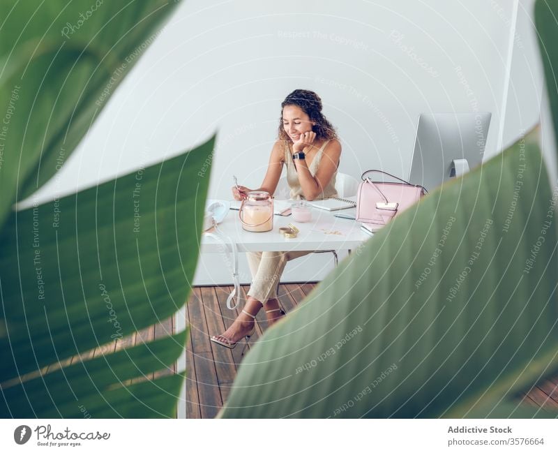 Smiling woman writing in notebook in office notes smiling leaves plant business work table leaning female palma de mallorca spain cheerful happy style elegant